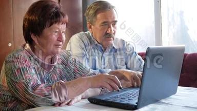 一对老夫妇坐在家里的笔记本电脑上。 女人看新闻，男人用手机说话